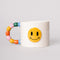 white ceramic mug with rainbow shapes handle and yellow smiley face on the front