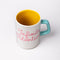 top view of yellow inside of ceramic mug with paper lines and pink cursive 'infinite potenial' typography across the front and light blue handle