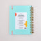 back view of sky blue 12-month large planner with white 'a joy to be around' and light pink elastic closure