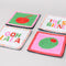 set of 4 beaded coasters: green beaded with cherry print, white with colorful beaded 'tres bien!', white with colorful beaded 'ooh lala', and pink with beaded olive.