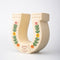 side view of cream horseshoe ceramic vase with colorful flower trim and 'best of luck' stamp in the center