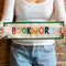 model holding canvas banner with rainbow 'bookworm' across the front and kelly green border