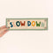model holding beige canvas banner with colorful 'SLOW DOWN' and sage green trim