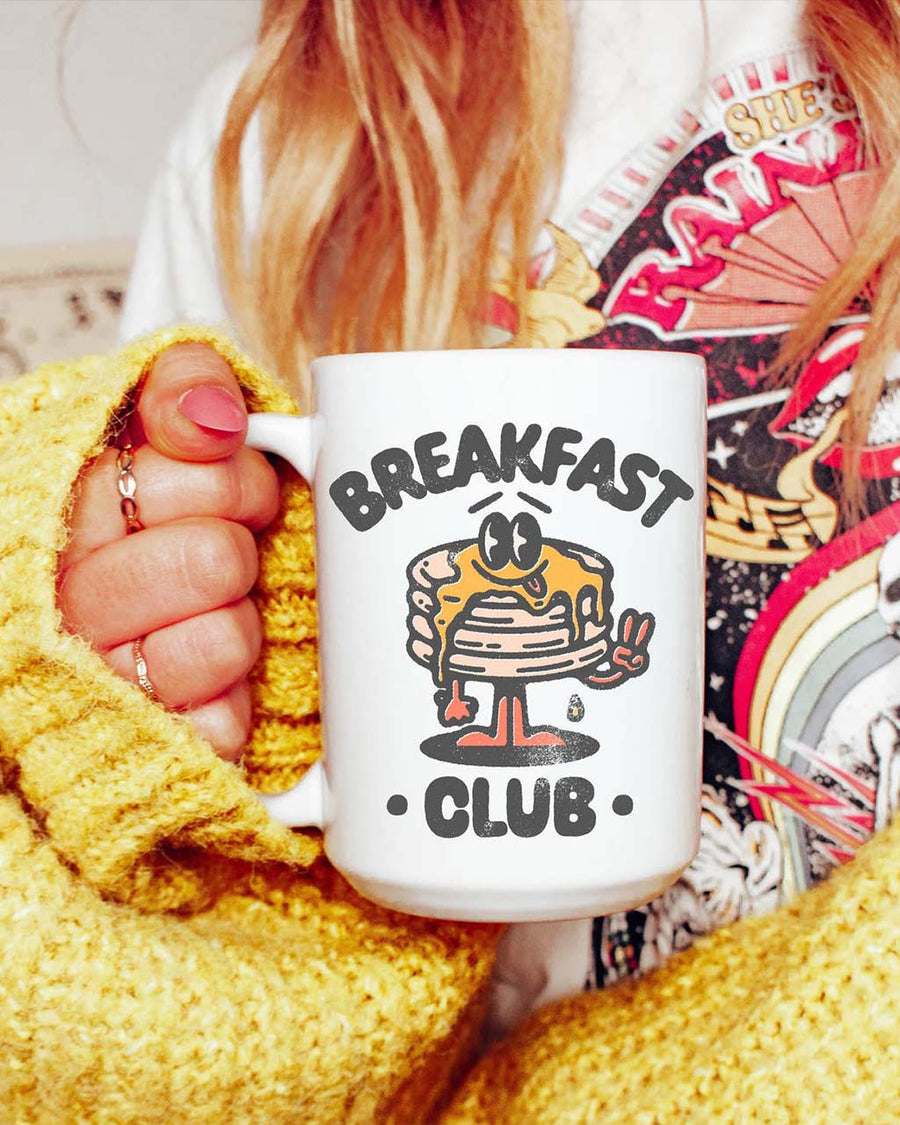 model holding 15 oz. white mug with smiley pancake stack and 'breakfast club' typography'