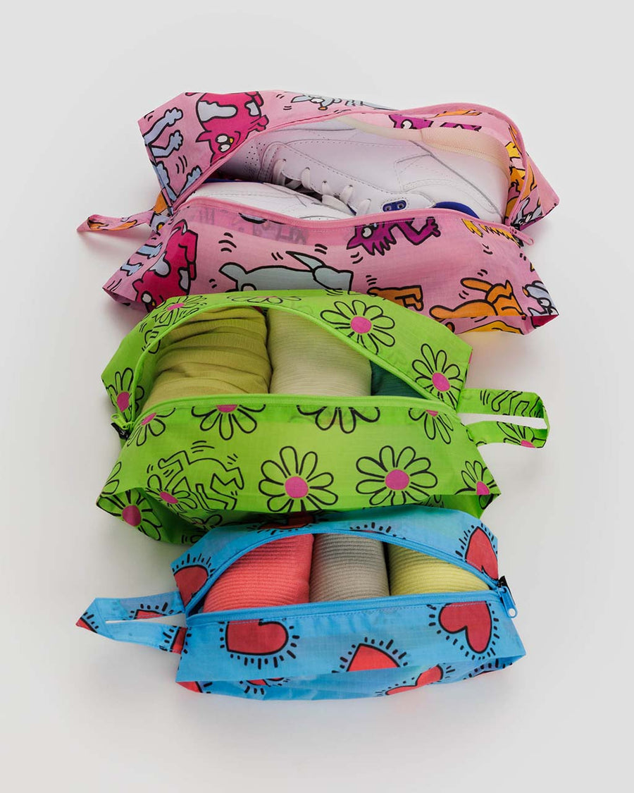 set of three keith haring print zip pouches: small blue hearts, medium green flowers, and large pink pets with items inside
