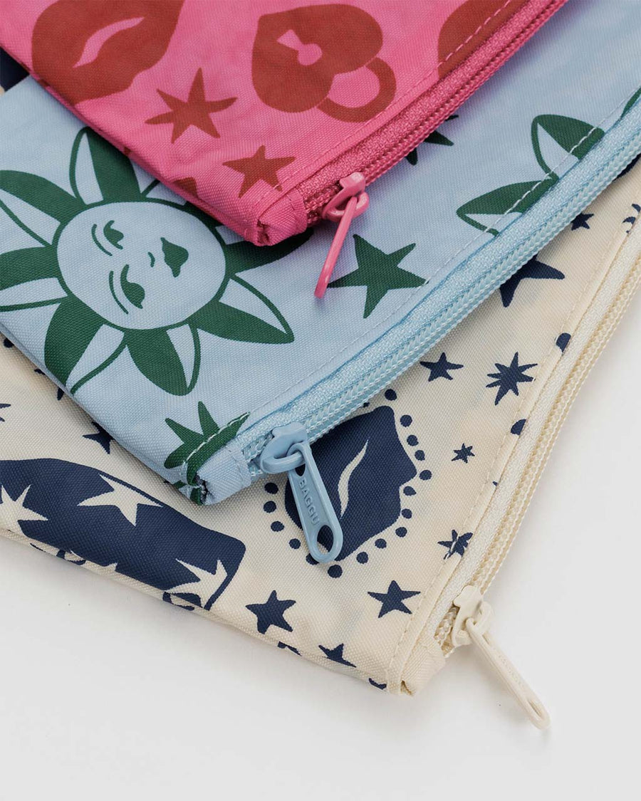 up close of zippers on set of three flat pouches: pink lip and lock, light blue sun face and moon and cream cherub and bow