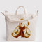 tan horizontal zip bag with teddy bear with a red bow around the neck