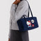 model carrying navy nylon bowler bag with embroidered hello kitty talking on a red phone