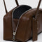 side view of model holding brown small dome recycled leather bowler bag with silver charm clasp