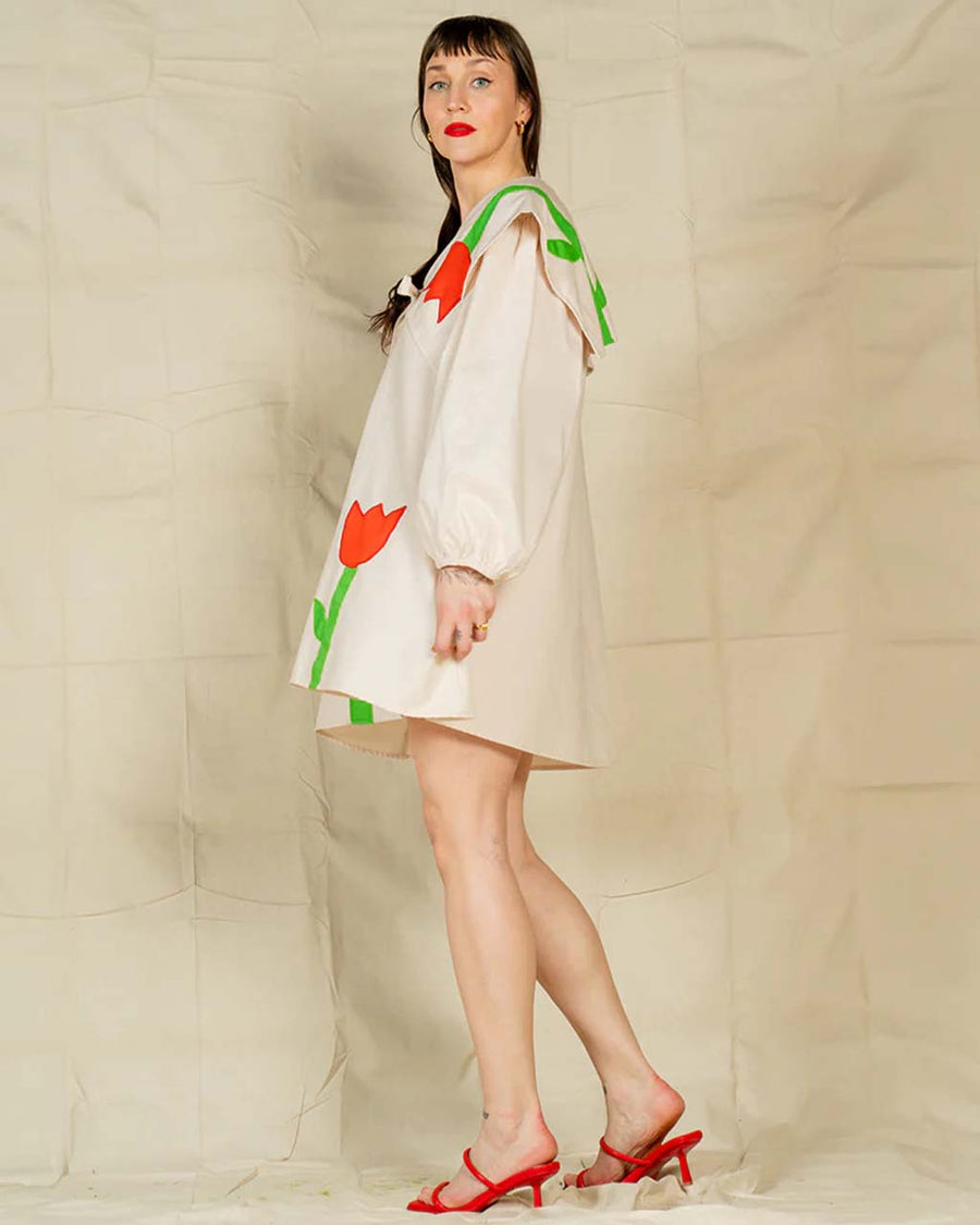 side view of model wearing cream mini dress with exaggerated collar, puff long sleeves and all over abstract tulip print