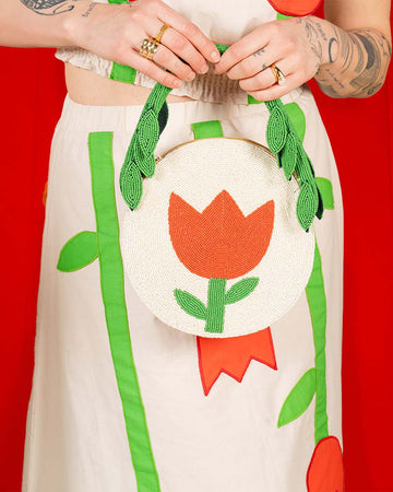 model holding cream round purse with red tulip and green beaded leaves on the strap