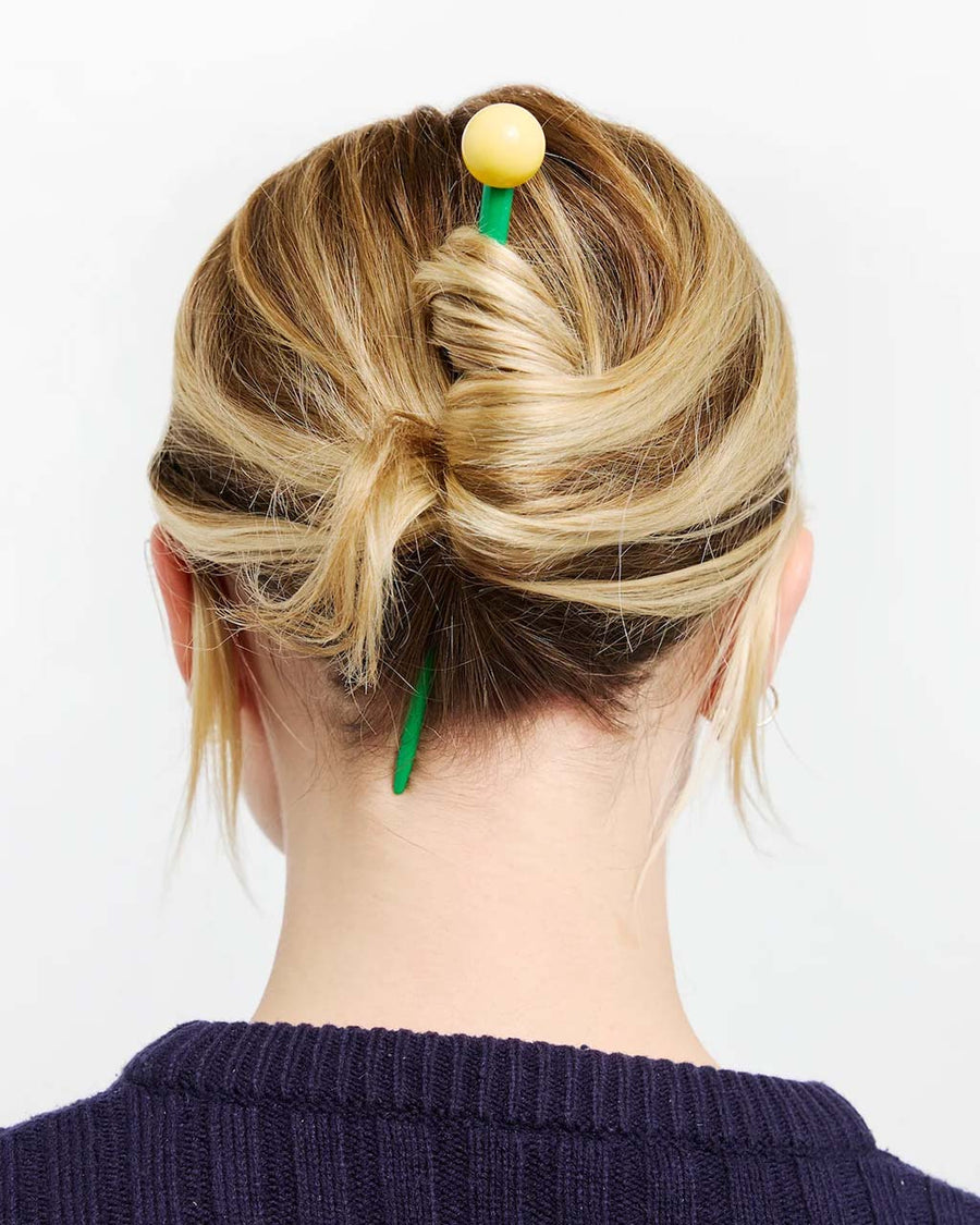 model wearing green hair stick with yellow ball on the end