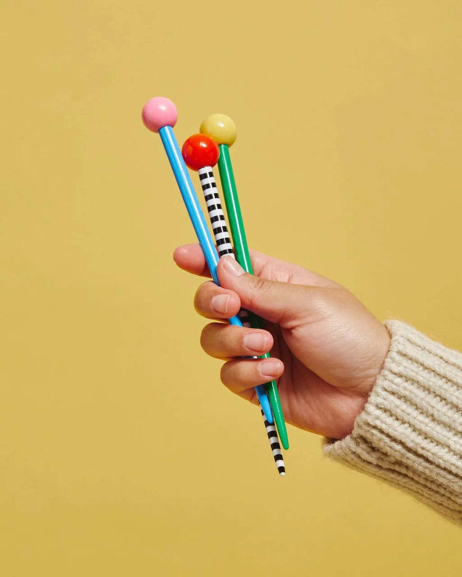model holding green hair stick with yellow ball on the end