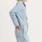 side view of model wearing light denim jumpsuit with button front, patch pockets, collar and long sleeves