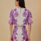 back view of model wearing white top with purple abstract floral print and wavy hems