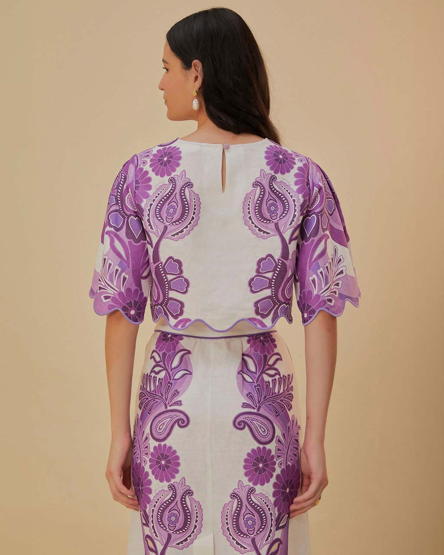 back view of model wearing white top with purple abstract floral print and wavy hems