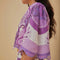 sideview of model wearing white top with purple abstract floral print and wavy hems