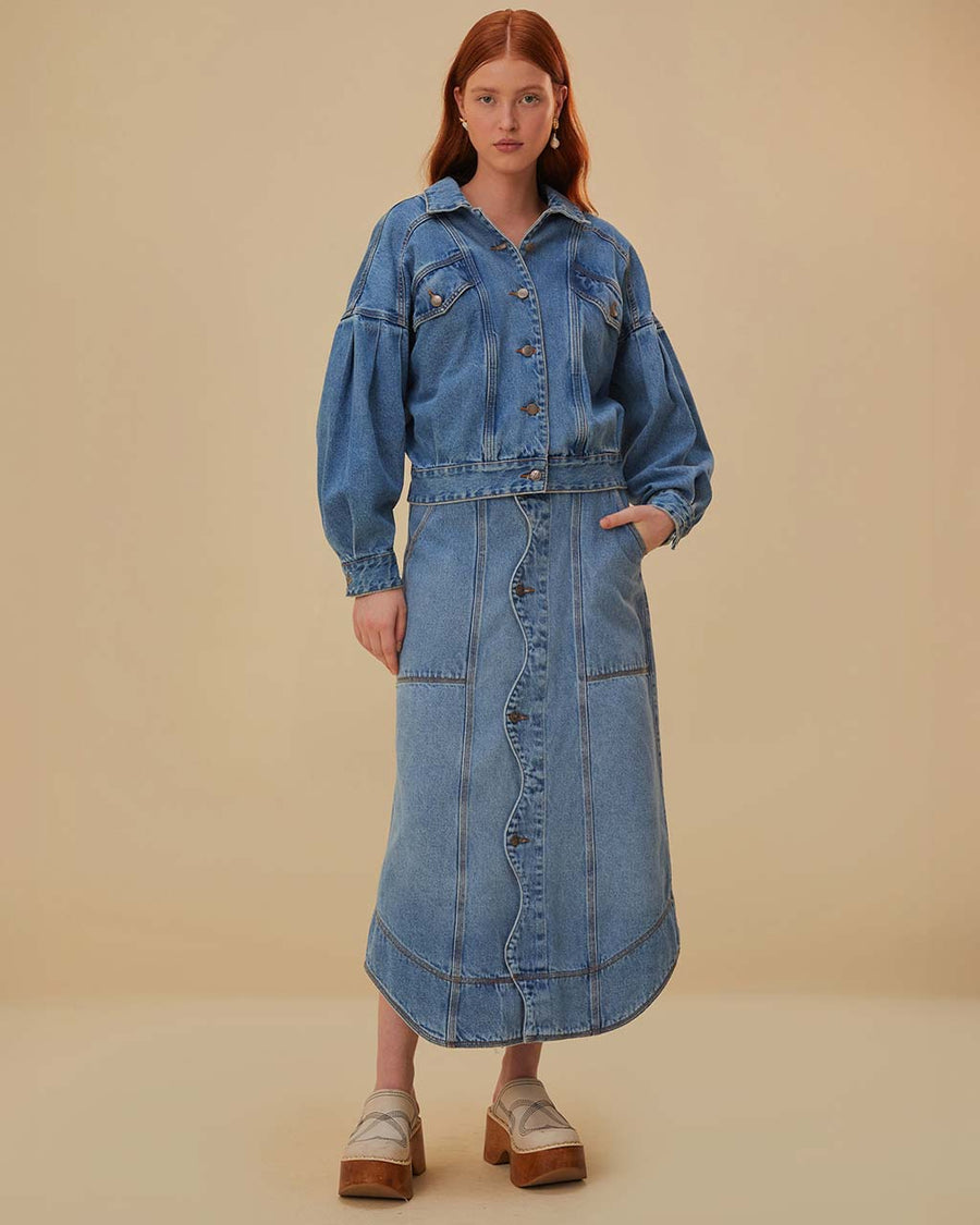 model wearing blue denim midi skirt with wavy button front, and exposed seaming