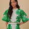 model wearing white cropped blouse with green abstract floral print and wavy hems