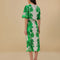back view of model wearing white midi skirt with green abstract floral print and wavy hems and matching blouse