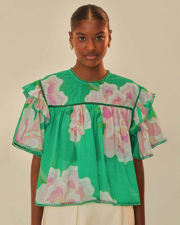 model wearing green flutter sleeve blouse with pink and white flowers, flutter sleeves and ric rac trim