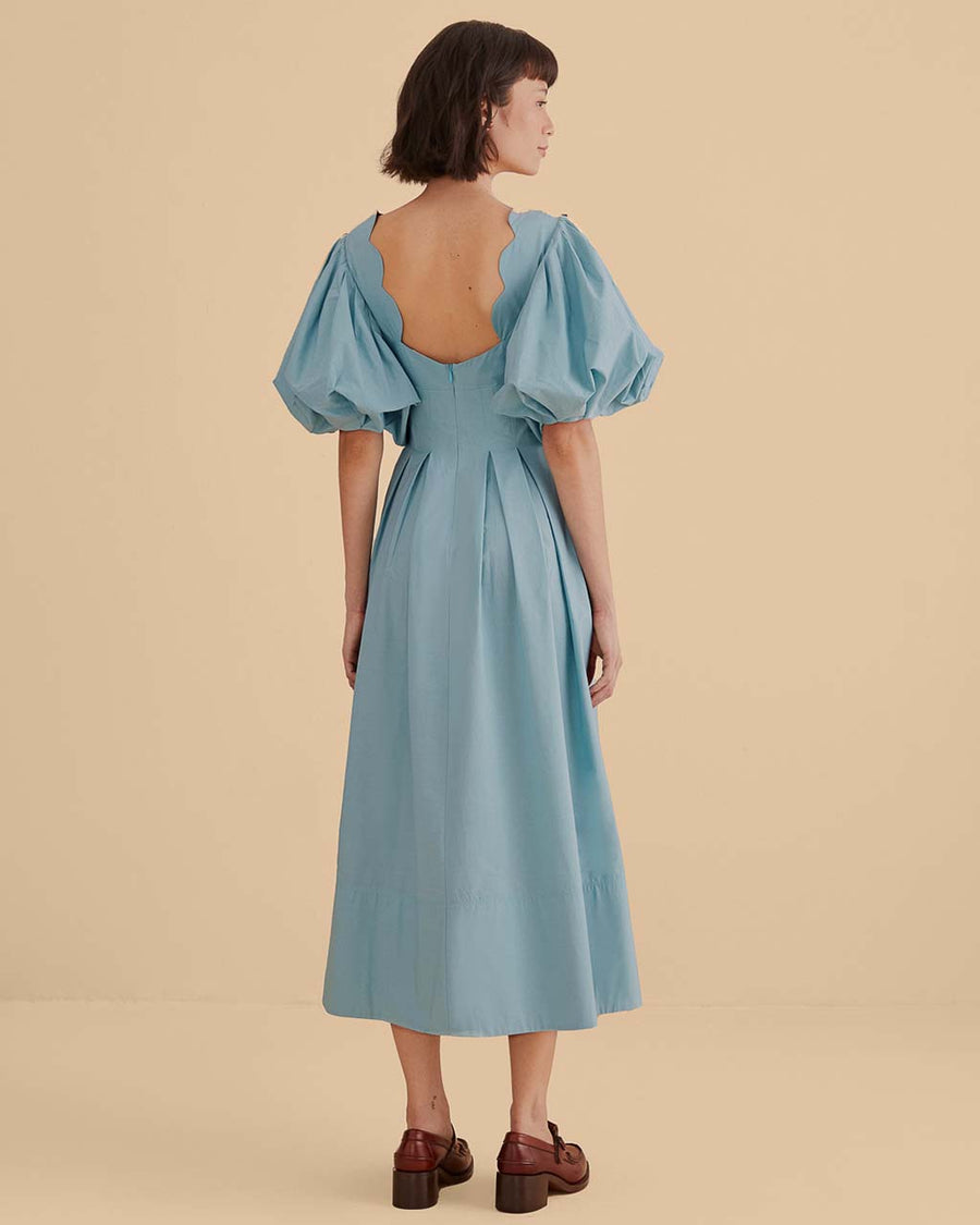 back view of model wearing icy blue midi dress with scalloped cut out and exaggerated puff sleeves
