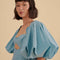 up close of model wearing icy blue midi dress with scalloped cut out and exaggerated puff sleeves