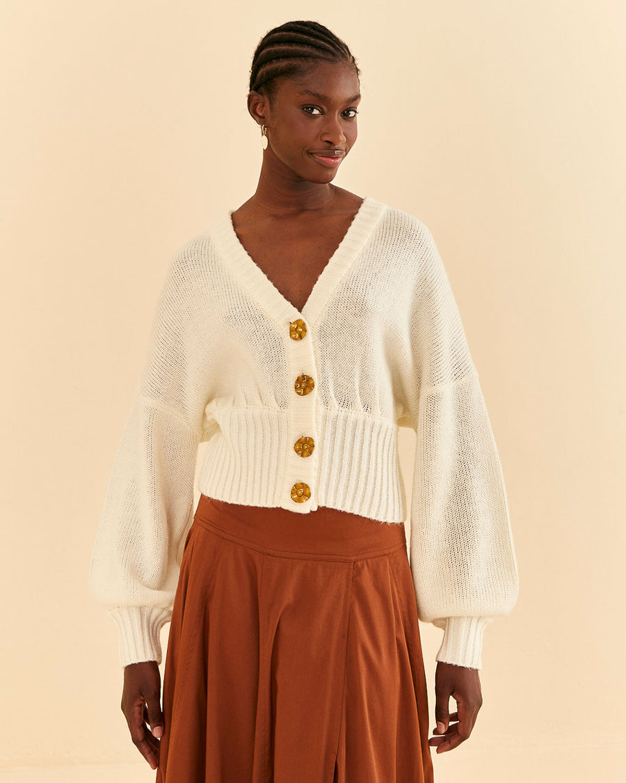 model wearing off white cropped cardigan with puff sleeves and large flower buttons