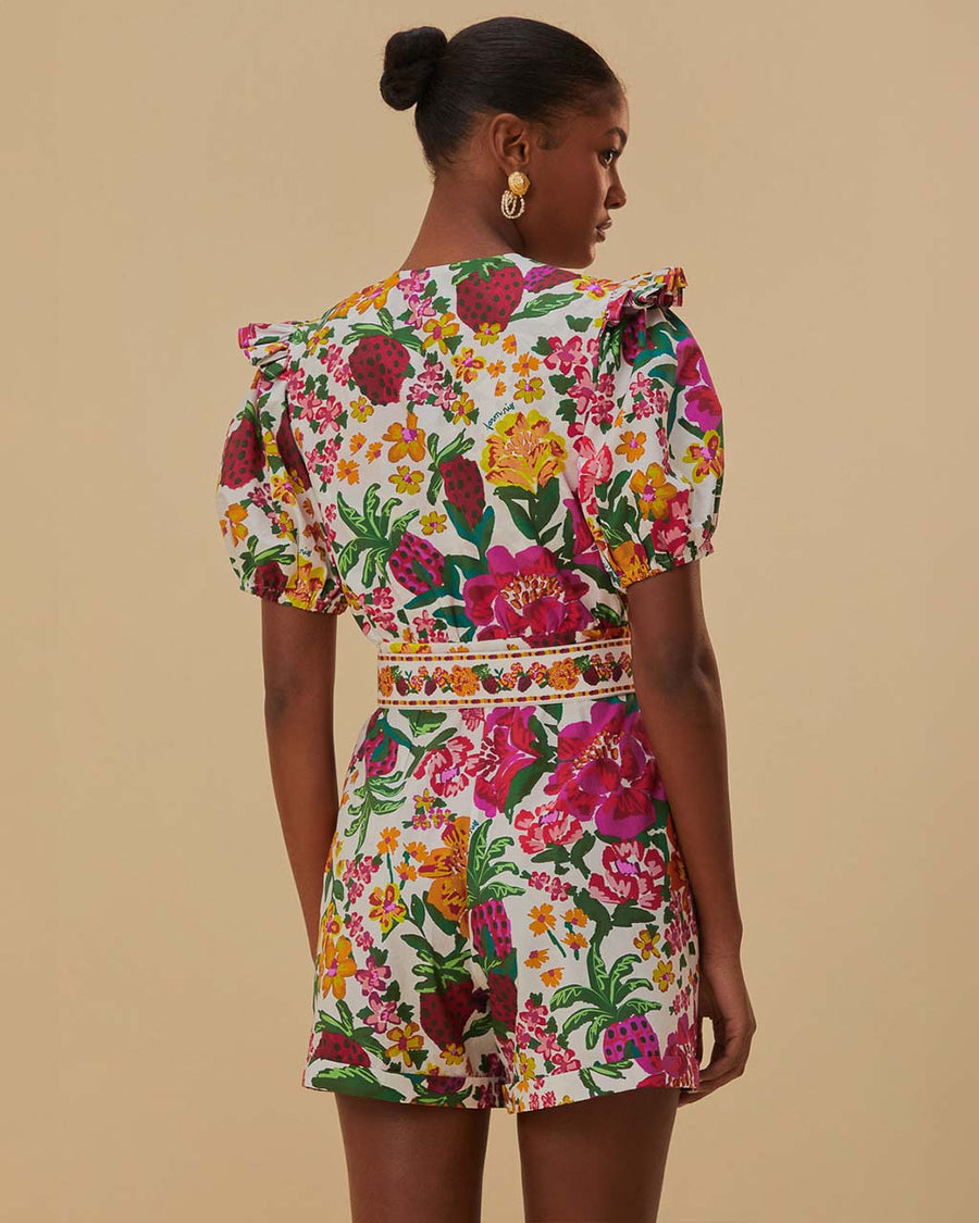 back view of model wearing white romper with colorful floral print, puff sleeves, and belt detail