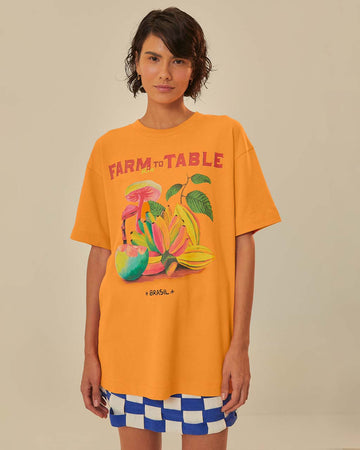model wearing orange oversized tee with colorful fruit graphic and 'farm rio to table' typography