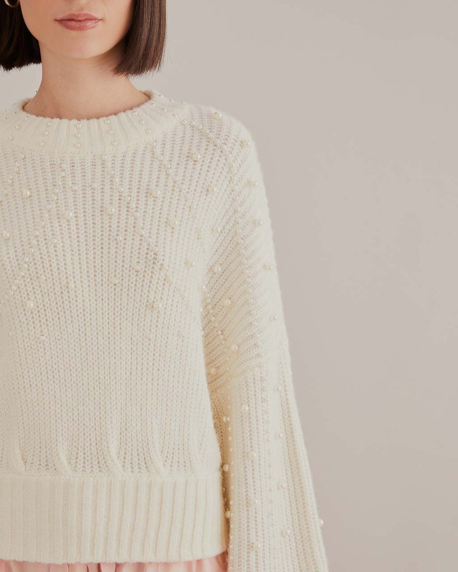 up close of model wearing white sweater with puff sleeves and pearl detail