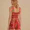 back view of model wearing cream and red abstract romper with tie waist and button front