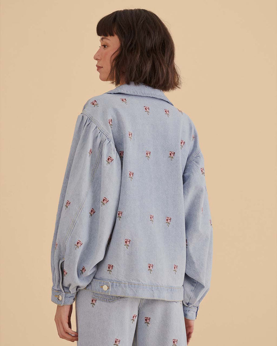 back view of model wearing light denim jacket with oversized collars and pink embroidered floral print