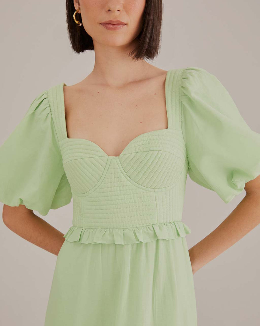 up close of model wearing soft green midi dress with ruffle hem and waist, puff sleeves and stitched corset bodice