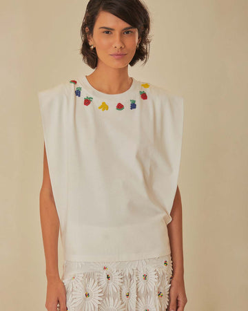 model wearing white muscle tank top with beaded fruit detail around the neckline