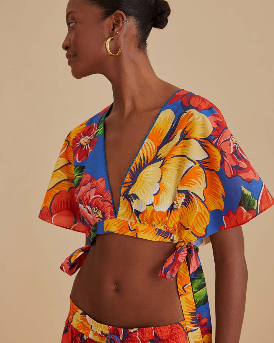 side view of model wearing blue cropped v-neck top with bold yellow, pink and red floral print and side ties