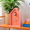 pink and orange vertical stripe house shaped alarm clock with white cuckoo on a shelf