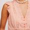 up close of model wearing peach button front tank with floral eyelets and flutter sleeves