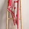 red triangle shawl with white folk floral print and white fringe hanging from a wooden ladder