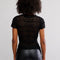 back view of model wearing black lace short sleeve top with leather pants