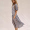 side view of model wearing pink and blue floral midi dress with tiered skirt, puffed short sleeves and blue trim on the neckline and sleeves