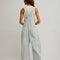 back view of model wearing relaxed fit blue and white railroad stripe overalls with a white tank