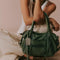olive green leather bag with two sets of straps and various zippers and zipper pulls