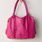back view of raspberry pink leather tote bag with several zipper pockets, double handles, and crossbody strap
