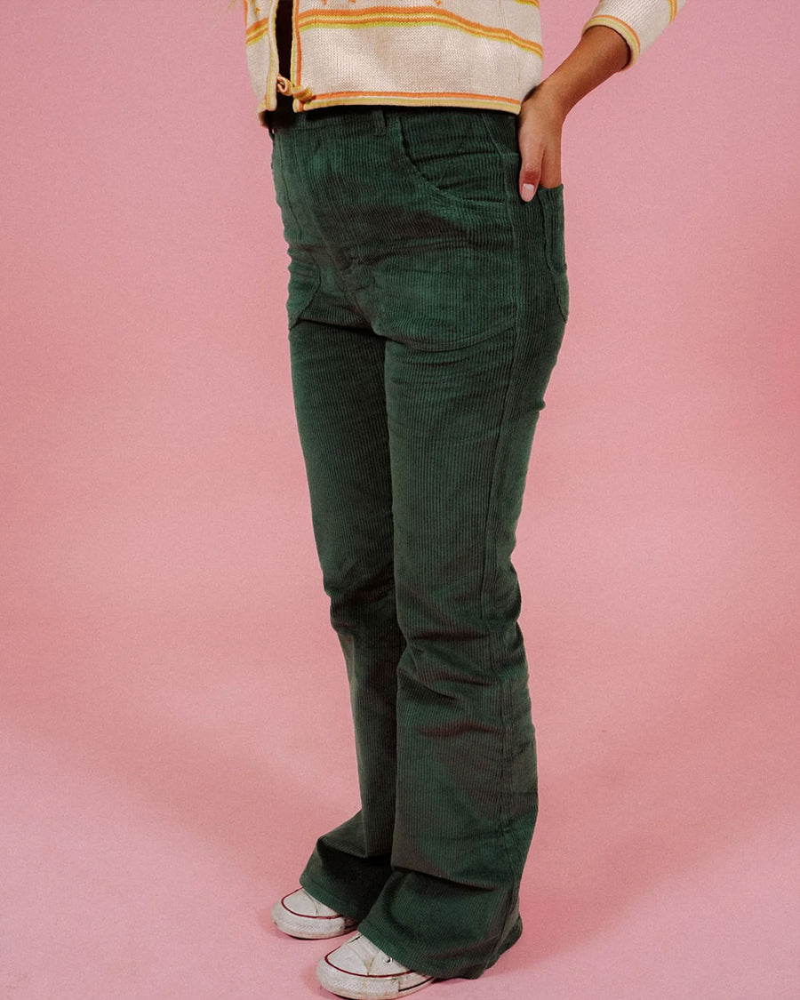 model wearing forest green corduroy bell bottoms with orange and yellow cardigan