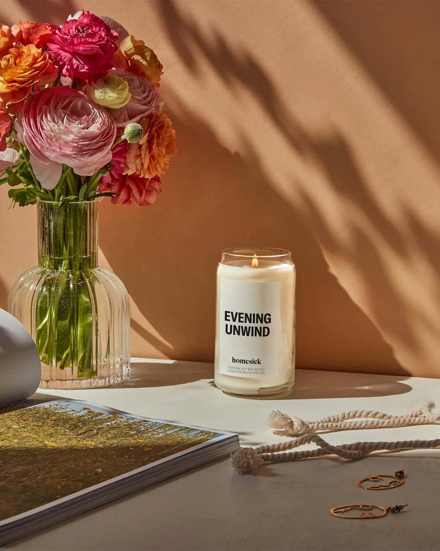 'evening unwind' 13.5 oz soy candle on table with a bouquet of flowers