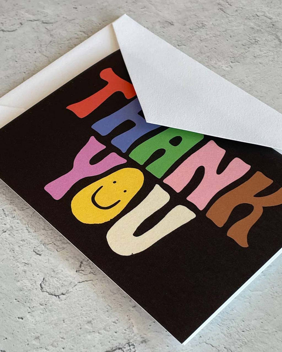 up close of thank you card set of 12 with black ground and wavy 'groovy' colorful 'thank you' with a smiley face