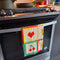 cream tea towel with strawberry, shamrock, banana, heart, house, pretzel, cherry, flower and bow icons hanging on an oven handle