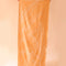 model holding up light orange sand resistant beach towel with white line sketched banana leaf print and has white tassels at each end