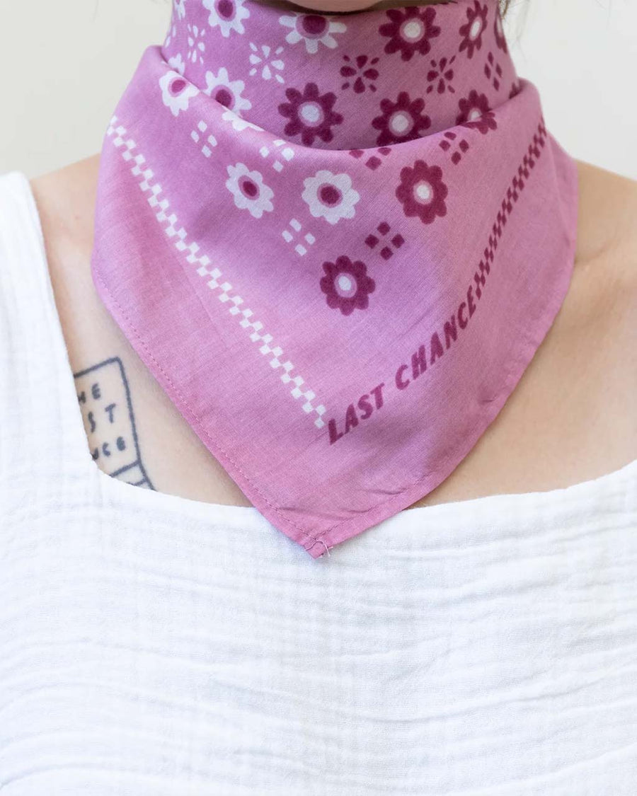 model wearing bright pink 22 in. x 22 in. square bandana with split white and plum floral print with knot in the back